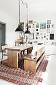 Wooden dining table with bench and chairs, pendant lights above, picture gallery on the wall