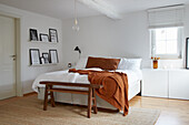 Bedroom with white bed, sideboard, framed art on shelves and wooden bench seat