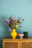Low sideboard with bouquet of flowers and bowl against blue wall