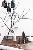 Zweige in Glasvase und kleine Weihnachtsbäume aus Pappkarton