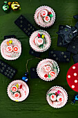 Weihnachtliche Cupcakes mit Zuckerdekor auf grünem Tisch mit Dominosteinen und Ornamenten