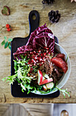 Salad with radicchio, pomegranate seeds and apple slices in a bowl on a wooden table