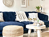 Blaues Sofa mit hellen Accessoires, Sitzpouf und Hocker mit Weißweingläsern im Wohnzimmer