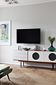 Sideboard below wall-mounted TV in living room with herringbone parquet floor