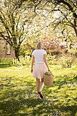 Blonde Frau in weißem T-Shirt und Rock mit Blumenkorb im frühlingshaften Garten