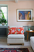 Armchair with decorative cushions, above modern painting on pale pink wall