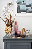 Artistic arrangement with feathers and heirlooms on sideboard below modern artwork on wall