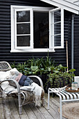 Rattan chair and metal stool on terrace outside black wooden house