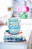 Stapel blauer und türkisfarbener Schalen und Tassen auf bunten Geschirrtüchern
