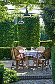 Round breakfast table with rattan chairs on the terrace, box trees in the background