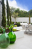 Elegante Terrasse mit Hochbeeten, grüne Ballonflaschen im Vordergrund