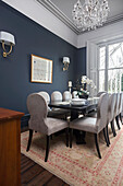 Black table and velvet upholstered chairs in dining room with blue wallpaper