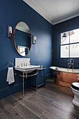 Vintage sink and copper bathtub in bathroom with dark blue walls