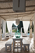 Ballonflasche auf Holzstisch und Bänke auf überdachter, mediterraner Terrasse