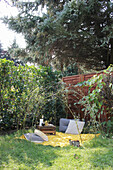Gelbe Picknickdecke mit Kissen und Holzkiste im Garten