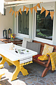 Yellow-painted wooden table with chairs and bench below bunting on terrace
