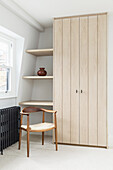 Built-in wardrobe with light wooden door and shelves in corner of room