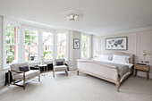 Sitting area and double bed in elegant, homely bedroom in beige tones