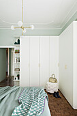 White corner wardrobes and double bed in bedroom with pale green walls
