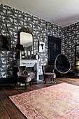 Upholstered chairs in front of disused fireplace in room with black and white Toile De Jouy wallpaper
