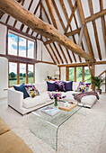 Corner sofa and glass coffee table in converted barn with wooden beams