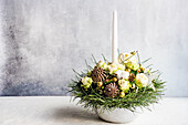 Christmas arrangement of fir branches, pine cones, white roses and one candle