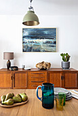 Blick über Esstisch auf Sideboard und Gemälde mit Meermotiv