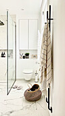 Elegantes, weißes Badezimmer mit Marmorfliesenboden und Glastrennwand