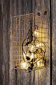 Industrielle Wandlampe mit Glühbirnen hinter Metallgitter an Holzwand