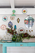 Wall decoration with colourful plates and mirror above blue console