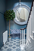 Eingangshalle mit blauen Wänden, gemusterten Fliesen, großem Spiegel und Treppenaufgang