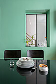 View over black table with a stack of plates on it and a green wall and interior window