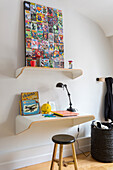 Minimalist desk, above it matching shelf with modern artwork on a white wall