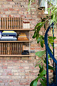 Antique books on a wall shelf on a brick wall with cascading hanging plants