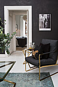 Anthracite-coloured armchair with golden frame in front of black wall with picture