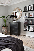 Bedroom with black chest of drawers, wall shelves, round mirror and plant decoration