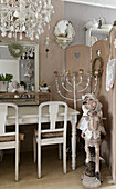 Alte Puppen auf Schaukelpferd und Kerzenständer neben weiß gestrichenem Holztisch, darüber Kronleuchter