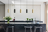 Modern kitchen island with black marble look, white wall tiles and pendant lights