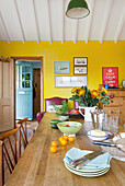 Essbereich mit gelbfarbener Wand mit gedecktem Holztisch und grüner Pendelleuchte