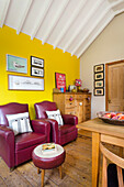 Dining area with yellow wall, red leather armchairs and leather stools