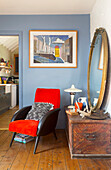 Vintage-Wohnzimmer mit blauer Wand, rotem Sessel, rundem Spiegel und antiker Truhe