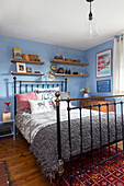 Metal bed with wall shelves in blue bedroom and wooden floor