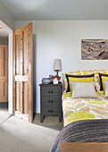 Schlafzimmer mit gelber Bettwäsche, Nachttisch und rustikaler Holztür
