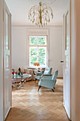 Blick in elegantes Wohnzimmer mit Fischgrätparkett, Mid-Century Couchtisch, türkisfarbenen Sesseln und Designer-Kronleuchter