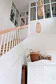 Hanging rattan lamps above white vintage cupboard next to staircase