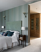 Modern bedroom with upholstered bed, wall lamps and patterned wallpaper