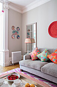 Wohnzimmer mit hellgrauer Couch, farbenfrohen Dekokissen und Tellern an der Wand