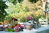 Geschirr, DIY-Lampenschirm und Krug mit blühenden Hortensien, die auf einem Couchtisch im Garten liegen