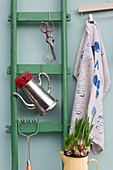 Green ladder, pair of old scissors, sieve, potato masher, two jugs, planted daffodil bulbs and coathanger with dish towel covered in various prints