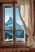 View of the Matterhorn peak through a window with a rustic wooden frame